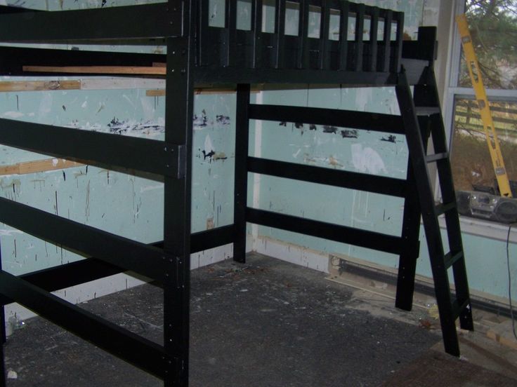 a black bunk bed sitting inside of a room next to a wall with peeling paint on it