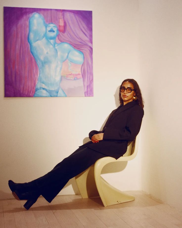 a woman is sitting on a chair in front of a painting and posing for the camera