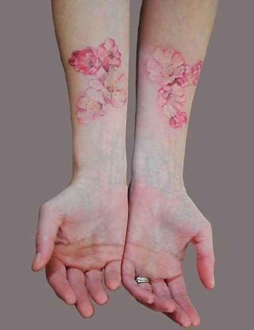 two hands with pink flowers tattooed on their arms, both holding each other's hand