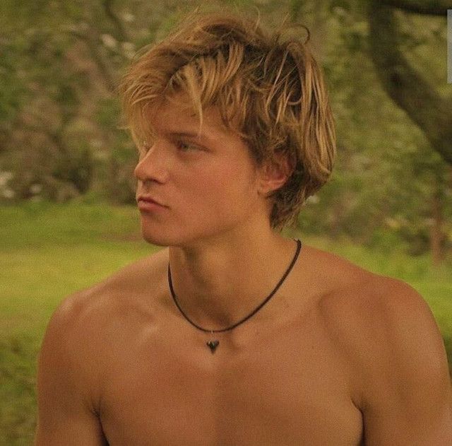 a shirtless young man with no shirt on standing in front of trees and grass