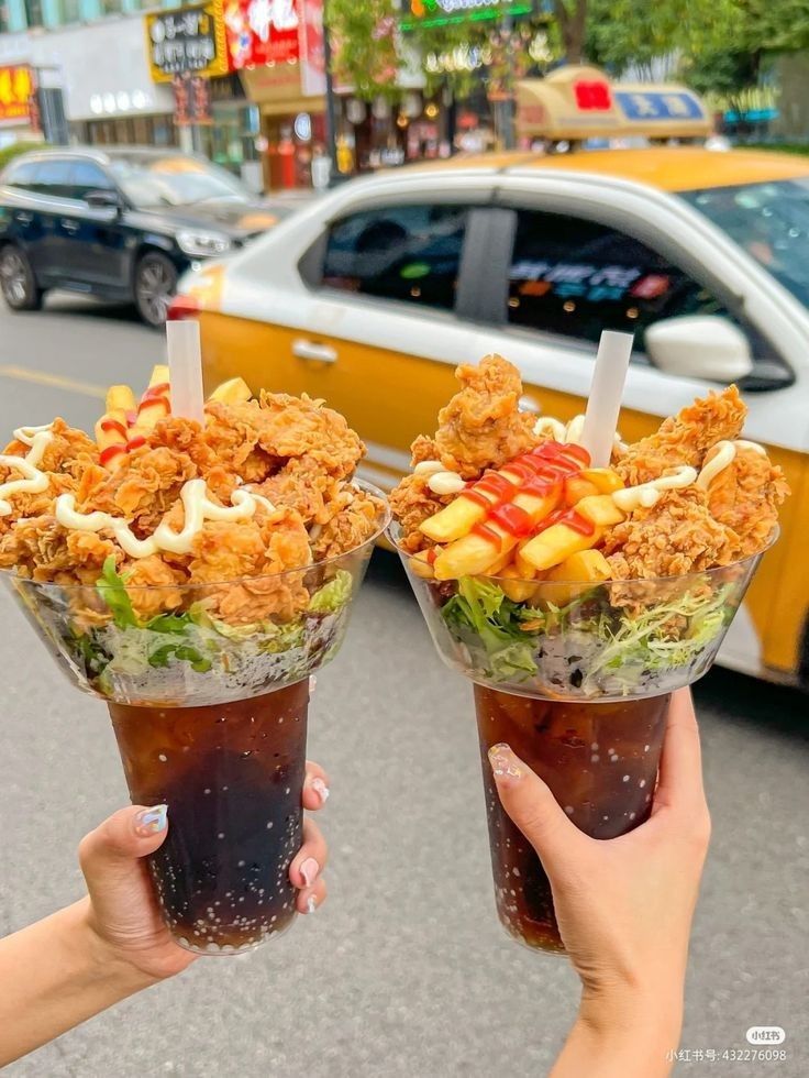 two people holding up cups filled with food on the side of a road next to a taxi