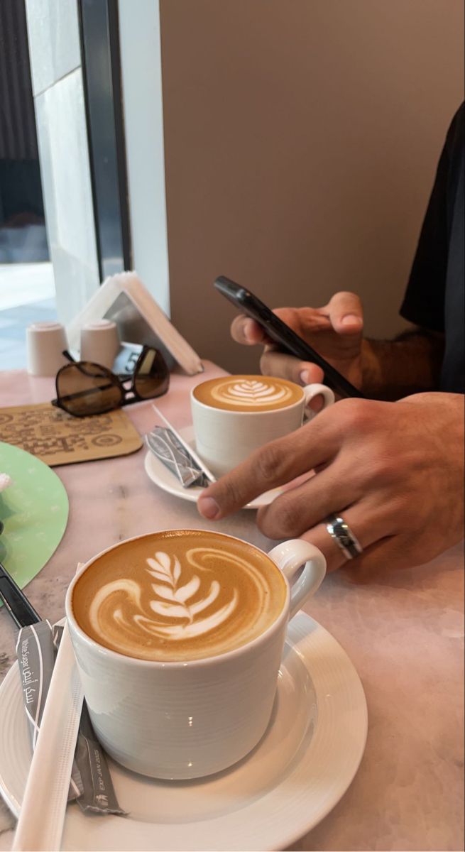 two people sitting at a table with cups of coffee and cell phones in their hands