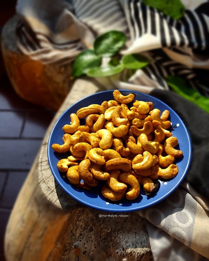 a blue plate filled with cashews sitting on top of a wooden table next to a potted plant