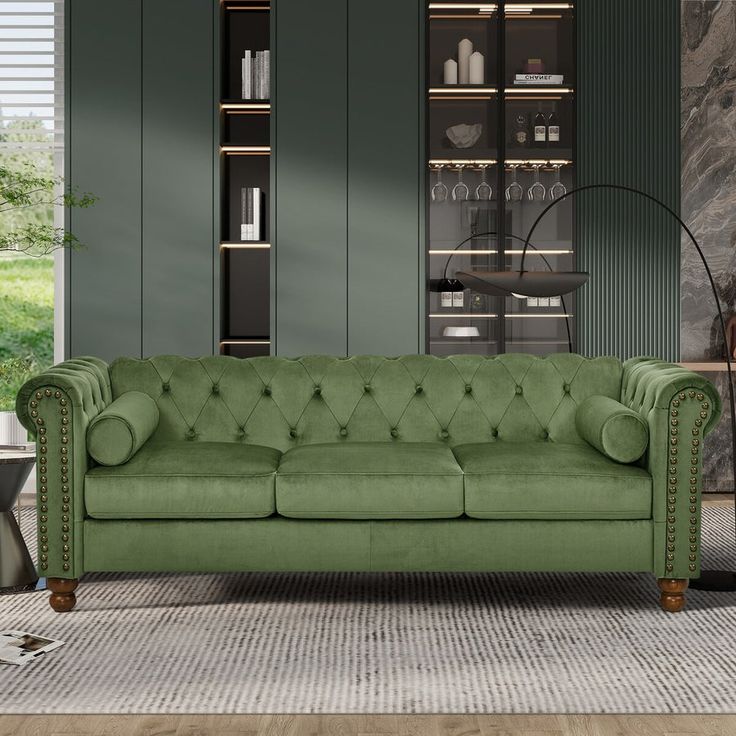 a green couch sitting in front of a tall book shelf filled with books and vases