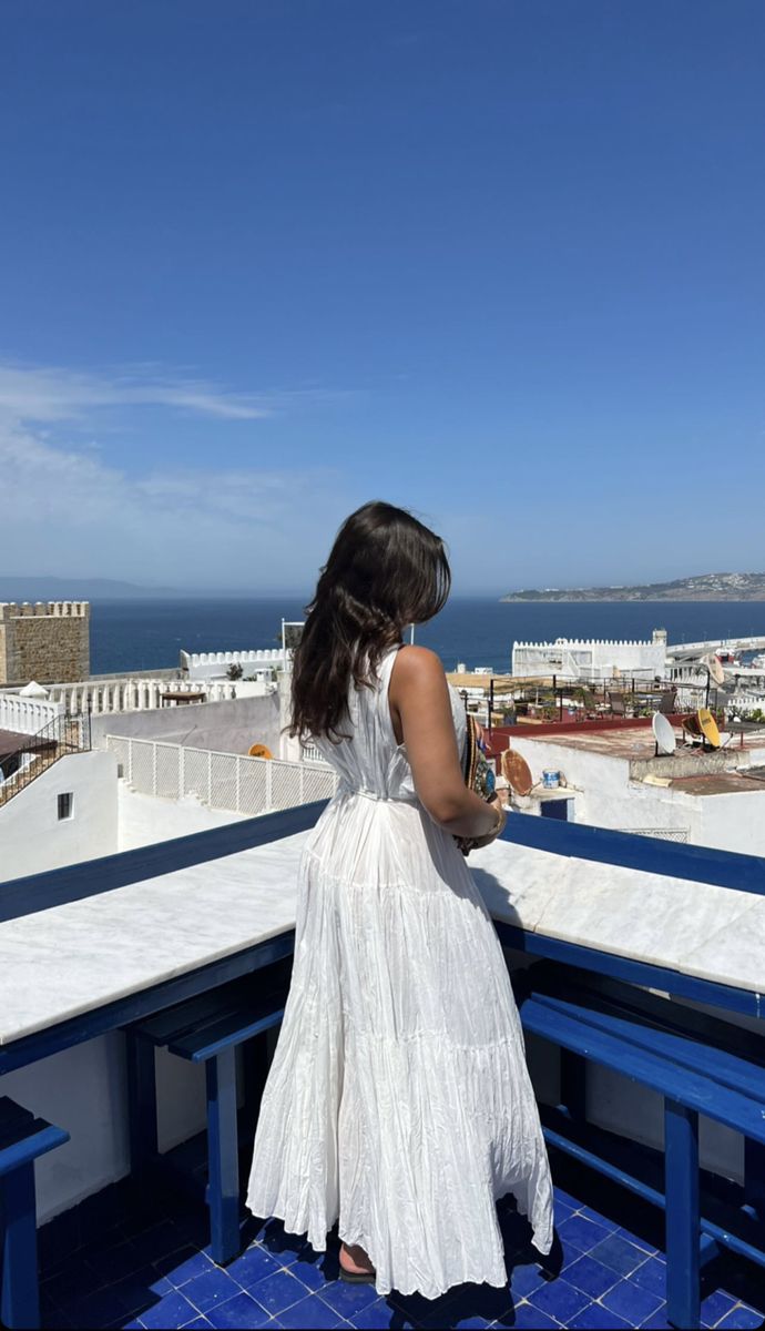 a woman standing on top of a blue and white building looking out at the ocean