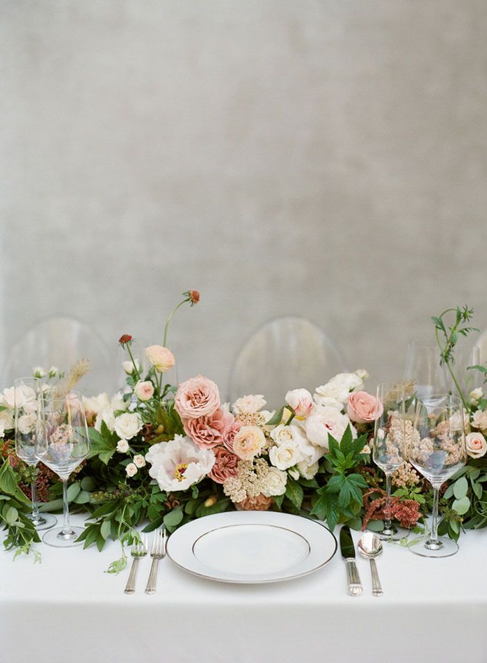 the table is set with white and pink flowers, greenery, and wine glasses