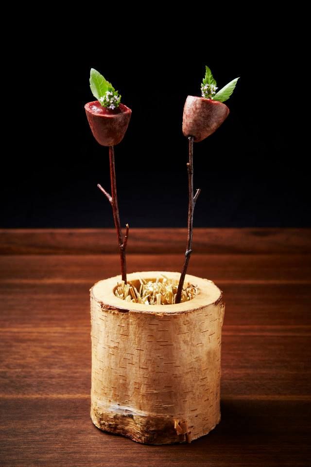 two small flowers are placed in a wooden container on a wood table with dark background