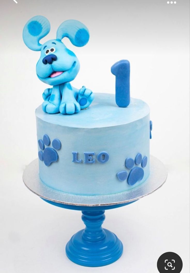 a blue cake with a dog on top and paw prints around the edges that says leo