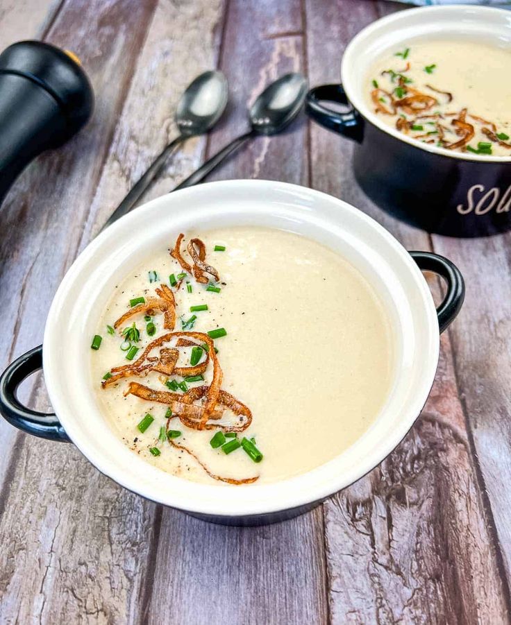 two white bowls filled with soup and garnished with green onions on a wooden table