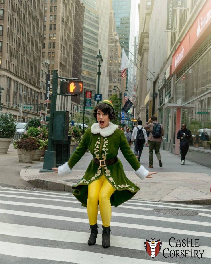 a woman dressed in green and yellow is crossing the street with her arms out wide