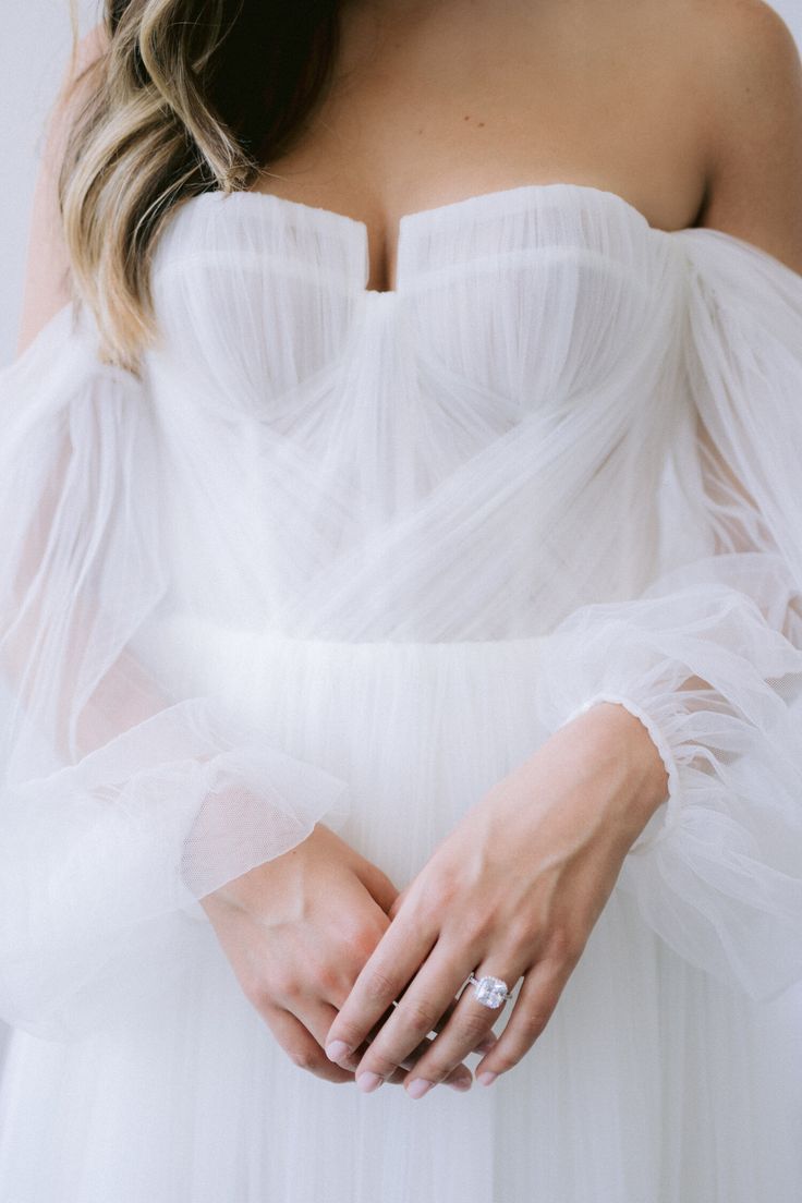 a woman in a white dress holding her wedding ring and wearing an off - the - shoulder gown