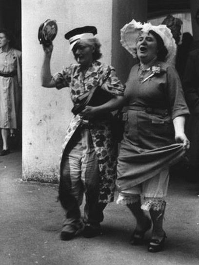 an old black and white photo of two women walking down the street with hats on