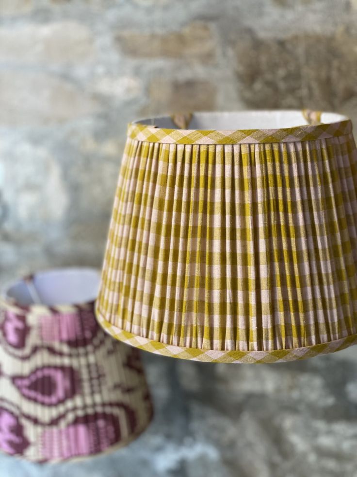 two lamps hanging from the ceiling in front of a stone wall and brick wall behind them