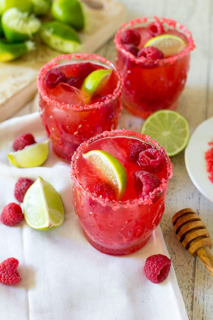 two glasses filled with raspberry margaritas on top of a white napkin next to lime slices