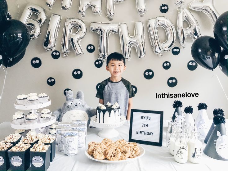 a young boy standing in front of a birthday cake and desserts on a table