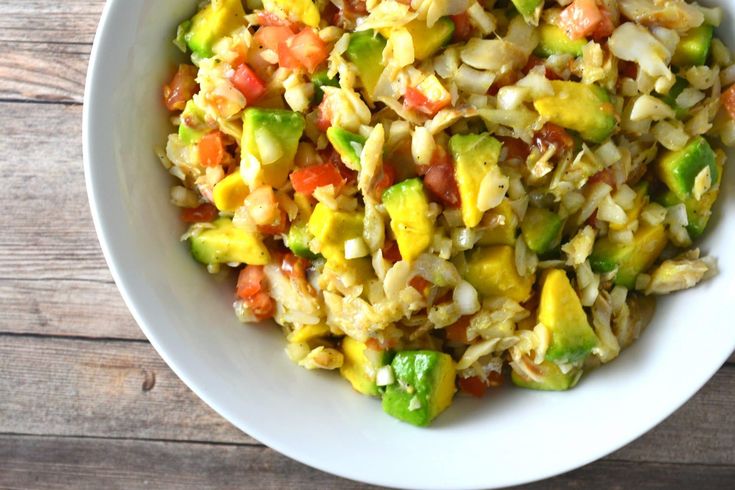 a white bowl filled with rice and vegetables on top of a wooden table next to a fork