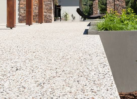 an outdoor patio with stone walls and plants in the foreground, surrounded by gravel