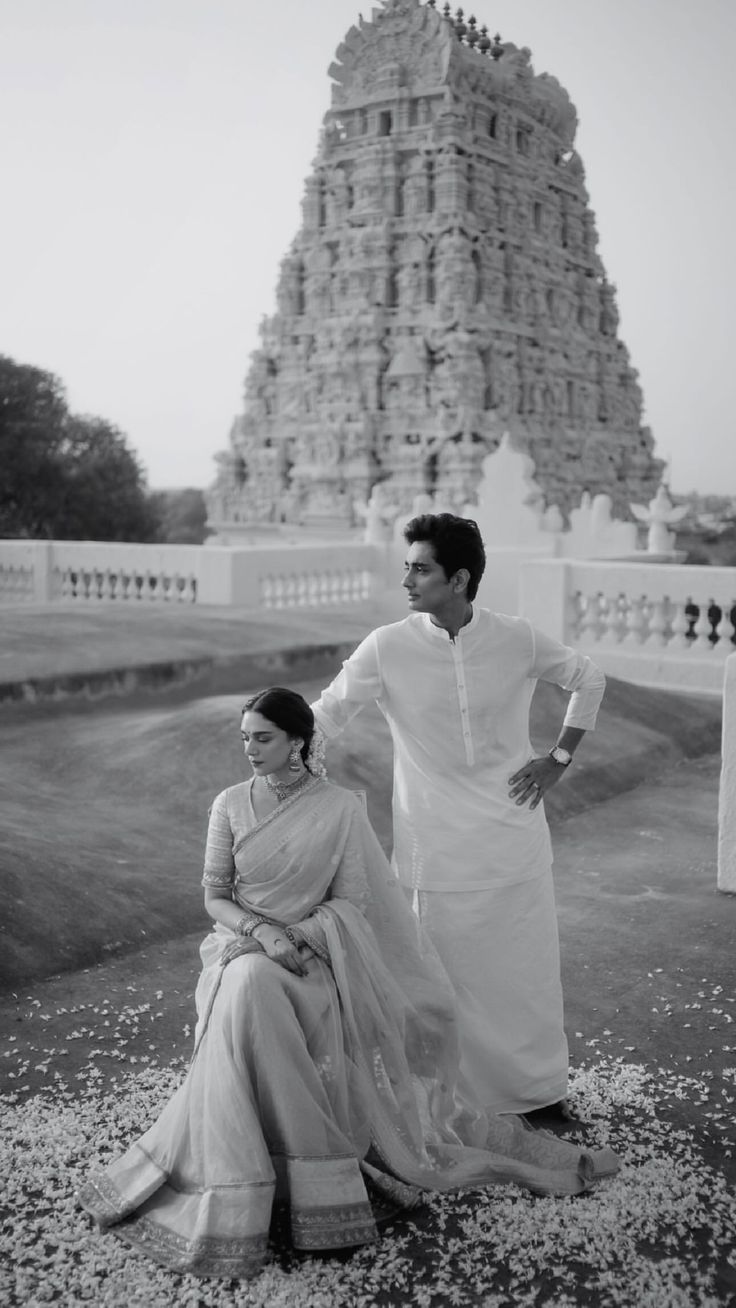 a man and woman standing next to each other in front of a tall tower with a clock on it