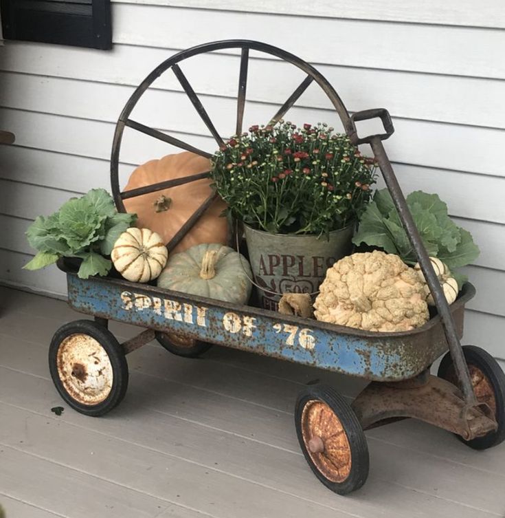 a wheelbarrow filled with pumpkins and gourds sits on the porch