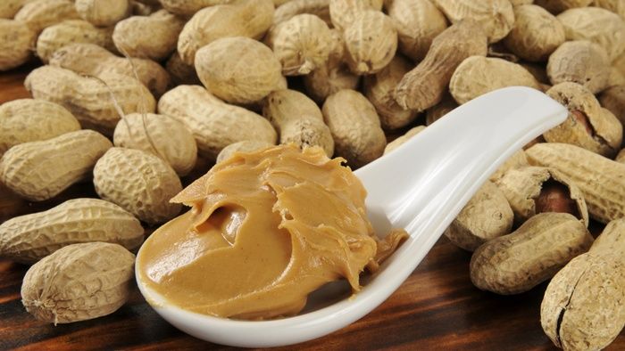 peanut butter in a spoon next to peanuts