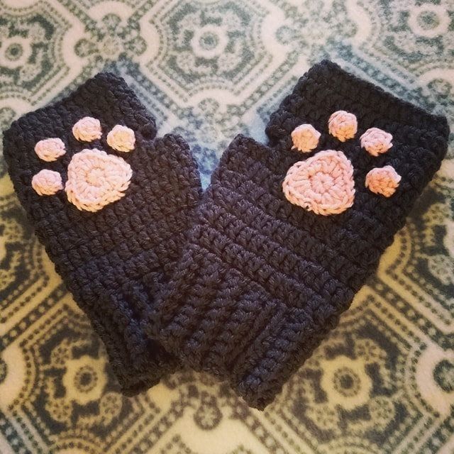 two crocheted mittens with paw prints on them sitting on a patterned surface