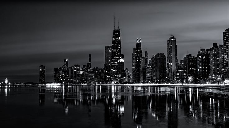 a black and white photo of the chicago skyline at night with lights reflecting in the water