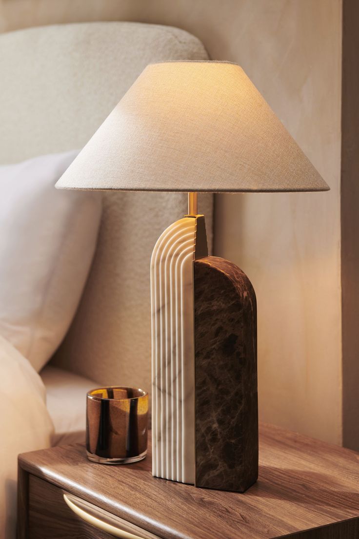 a lamp on a night stand next to a nightstand with a bed in the background