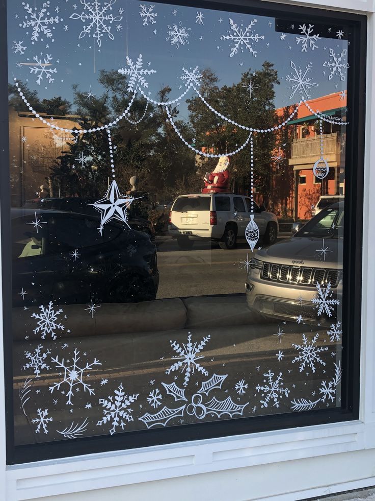 the window is decorated with white snowflakes and christmas decorations, while cars are parked outside