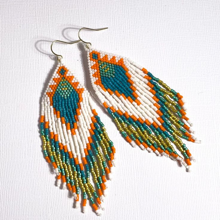 Incredible boho southwest style earrings in cream, orange, and sea blue. All of our earrings are handmade by women in the Philippines working their way out of poverty earning fair wage. Materials - glass beads, 14K gold hook Measurements - 4 1/4” L x 1” W including hook Bohemian Fair Trade Orange Jewelry, Fair Trade Bohemian Orange Jewelry, Fair Trade Orange Bohemian Jewelry, Orange Bohemian Earrings With Large Beads, Artisan Handwoven Orange Earrings, Bohemian Orange Earrings With Large Beads, Artisan Orange Handwoven Earrings, Orange Bohemian Handwoven Jewelry, Orange Teardrop Bohemian Beaded Earrings