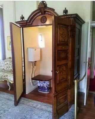 an old wooden cabinet is open to reveal a toilet in the corner with a lamp on it