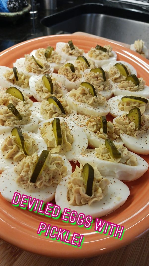 an orange plate topped with deviled eggs and pickles on top of a wooden table