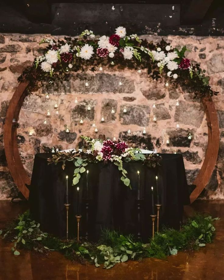 a table with candles, flowers and greenery on it in front of a brick wall