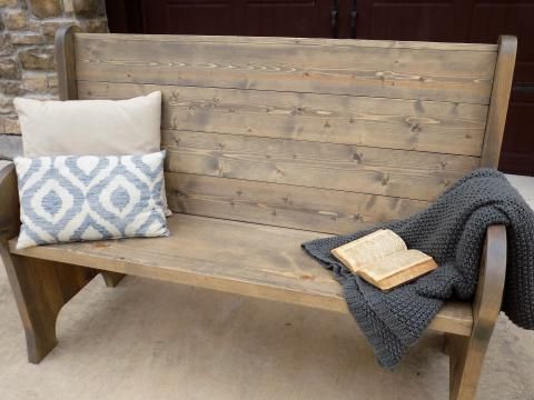 a wooden bench sitting on top of a sidewalk next to a book and pillow with a blanket