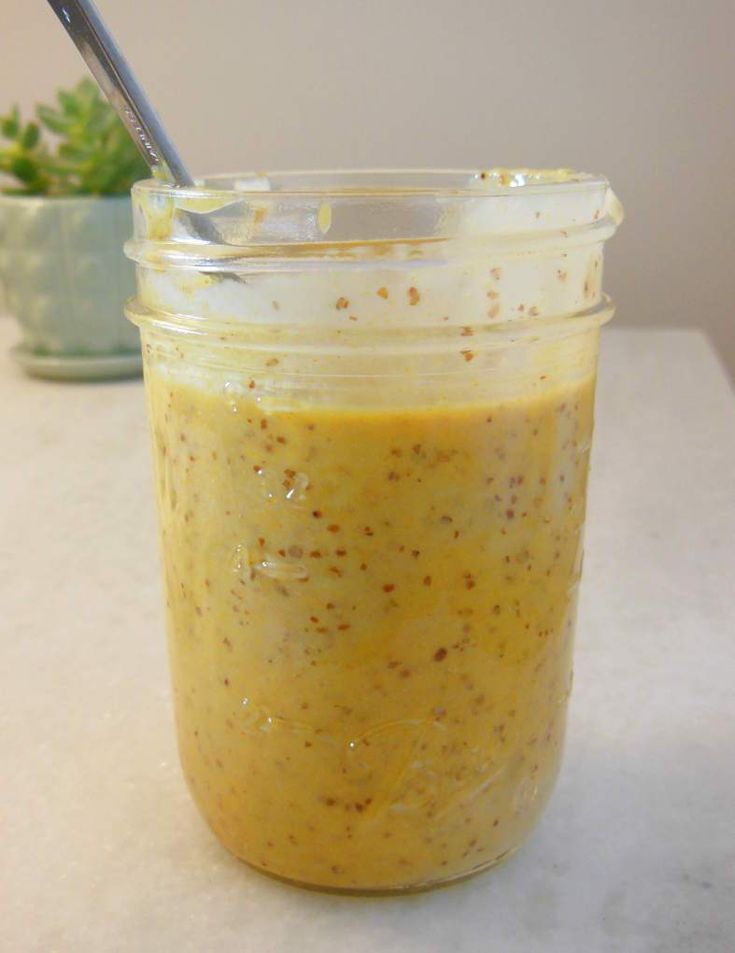 a jar filled with yellow liquid sitting on top of a table next to a potted plant