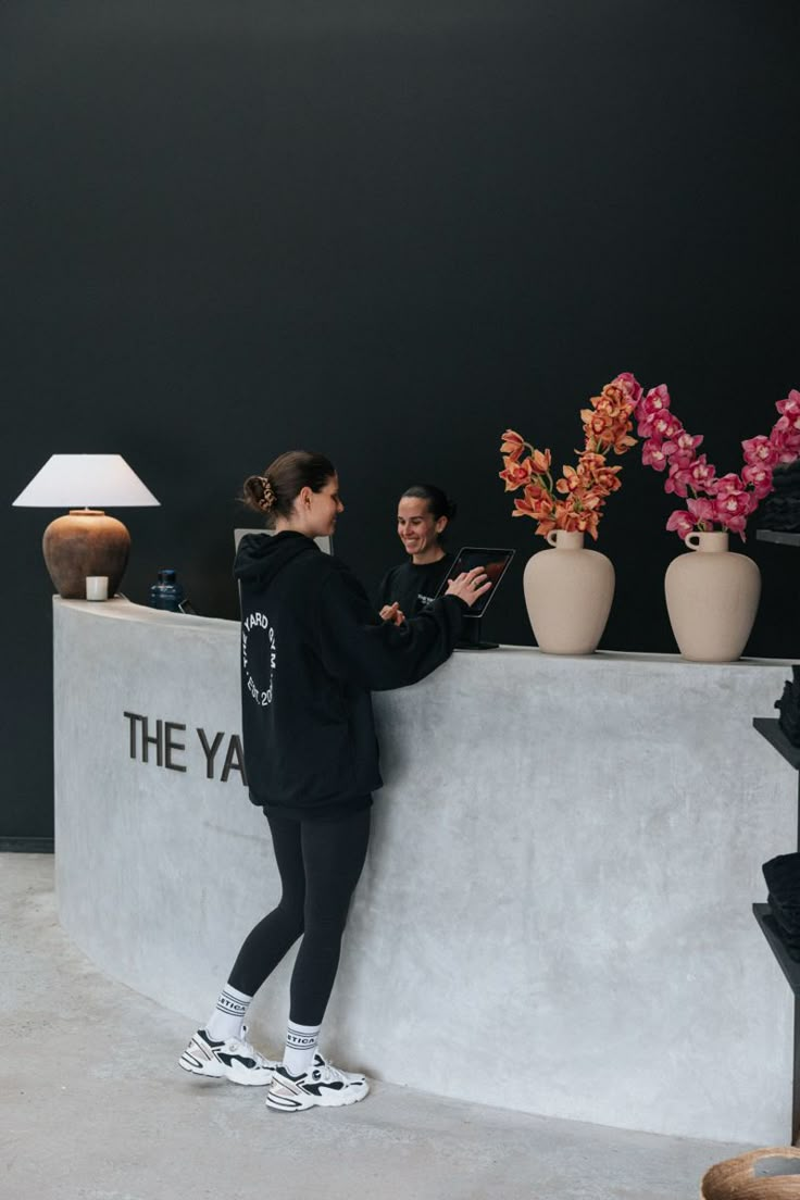 two women standing next to each other in front of a wall with flowers on it