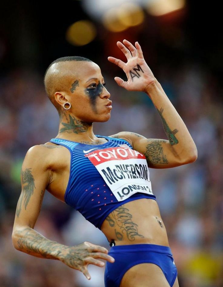 a female athlete with tattoos on her body and hands up in the air while wearing a blue outfit