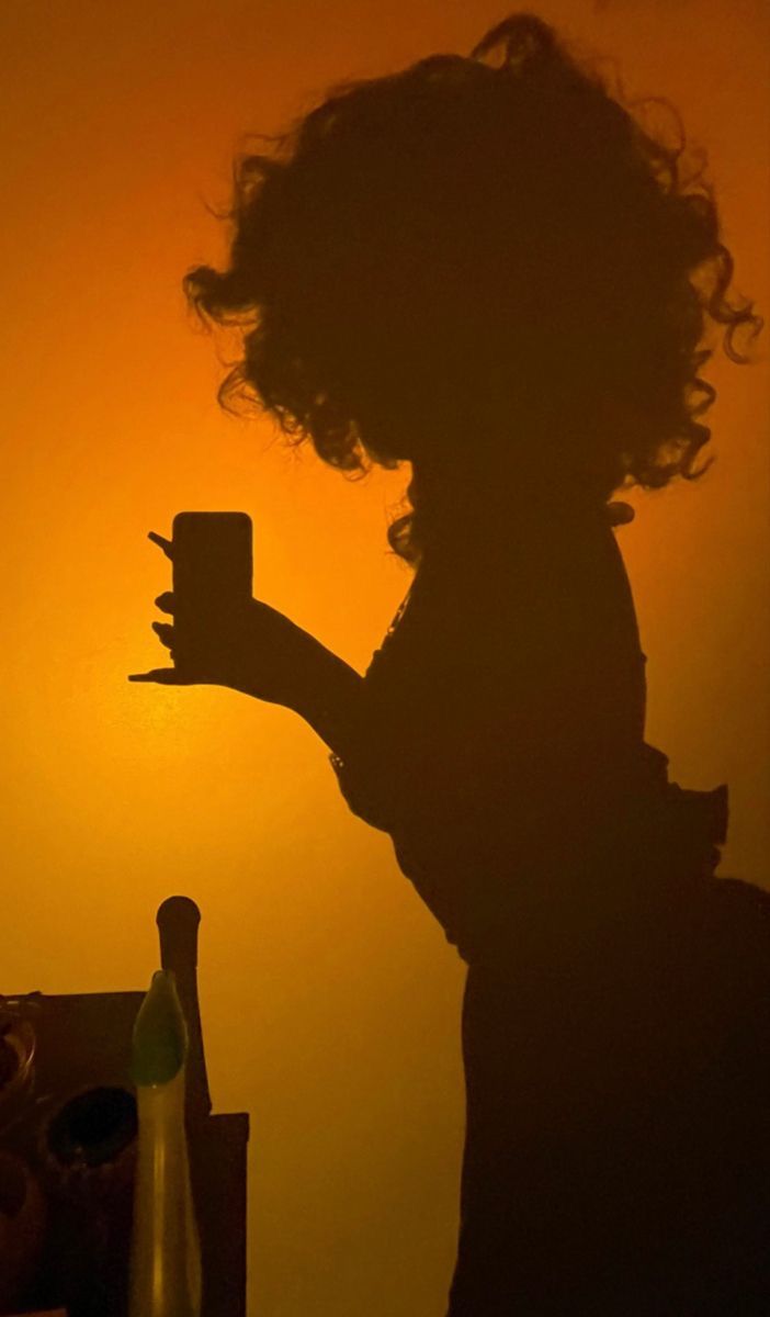 the silhouette of a woman holding a cup in front of an orange and yellow sky