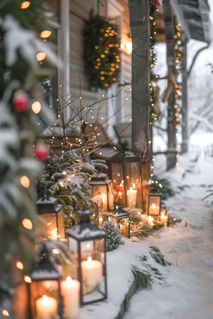 candles are lit outside in the snow next to a house with christmas decorations on it