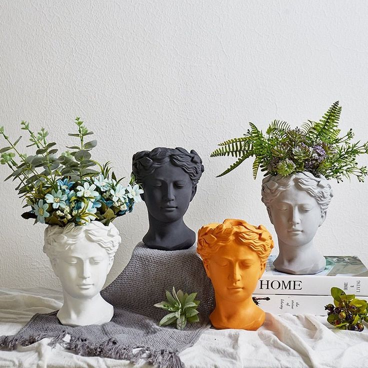 three ceramic head vases with plants in them sitting on a table next to books