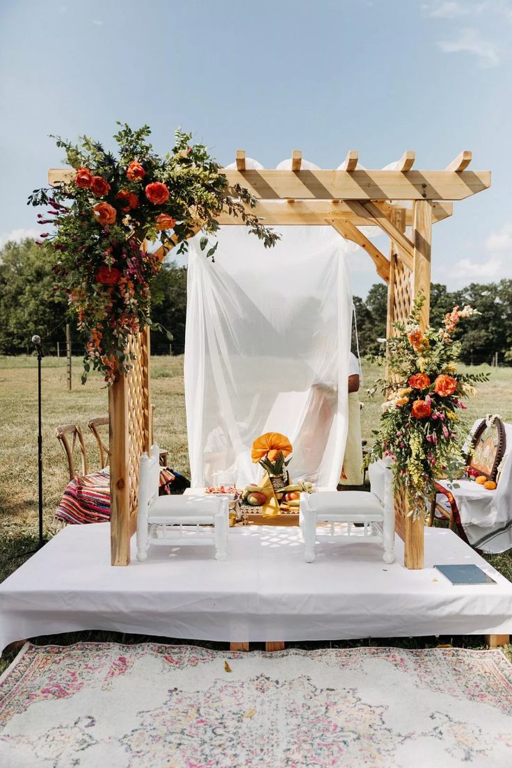 an outdoor ceremony setup with flowers and greenery on the table, in front of a white drape