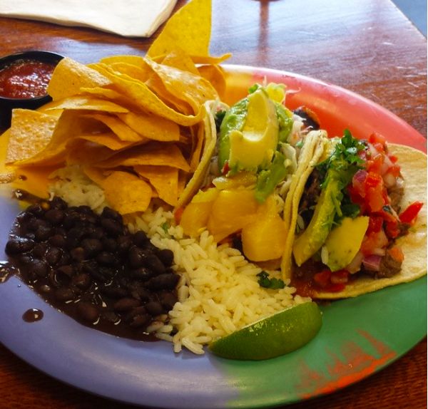 a plate filled with tacos, rice and beans on top of a wooden table