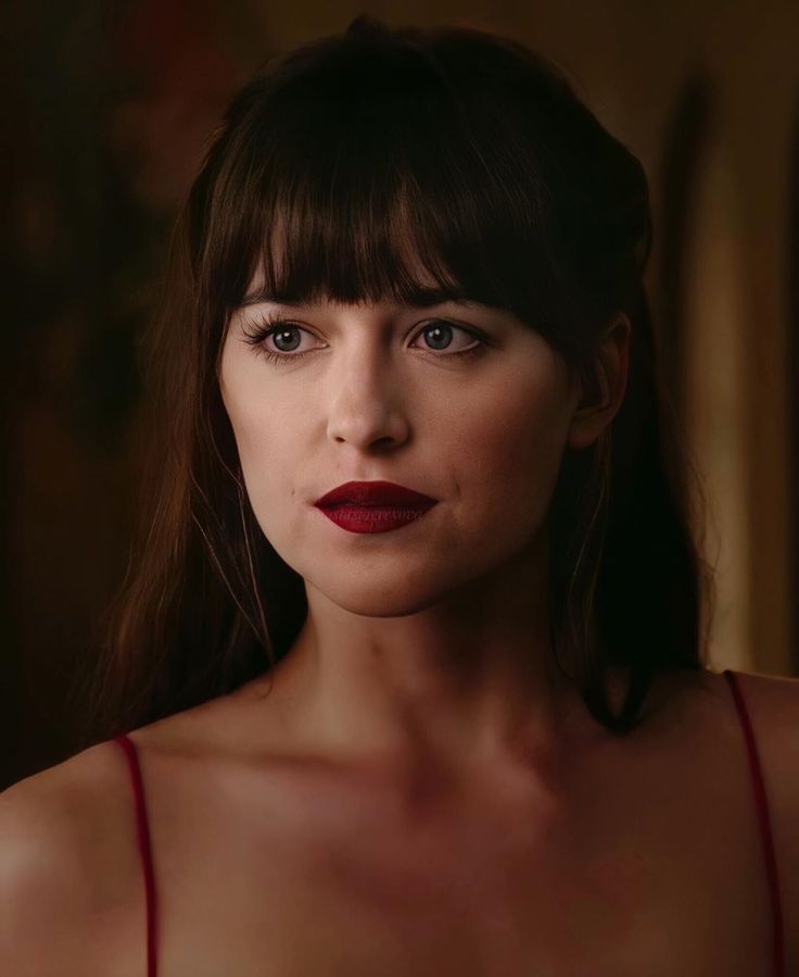 a woman with dark hair and red lipstick in a dimly lit room looking at the camera