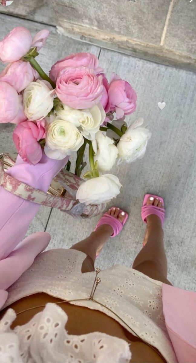 a woman's feet with pink and white flowers in a vase on the ground