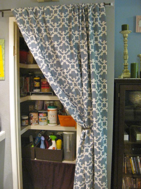 an open pantry door with the curtains pulled back to reveal shelves and storage bins