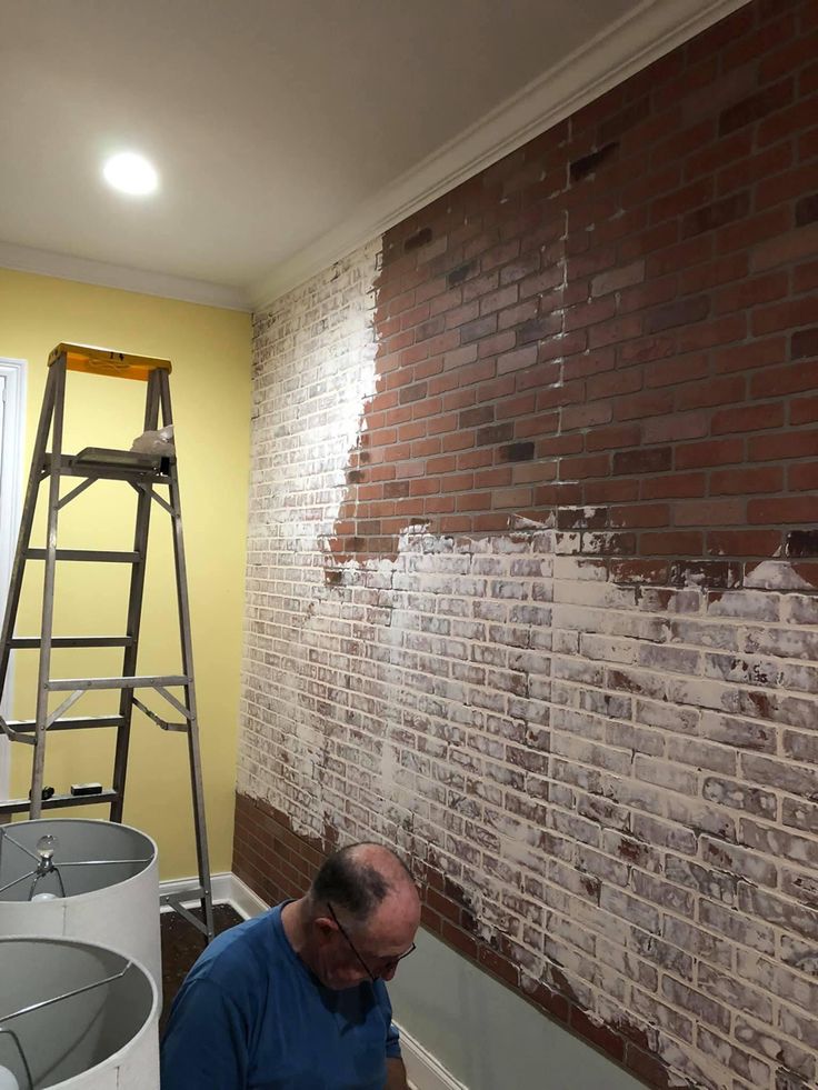 a man is painting a brick wall in an empty room with a ladder on the side