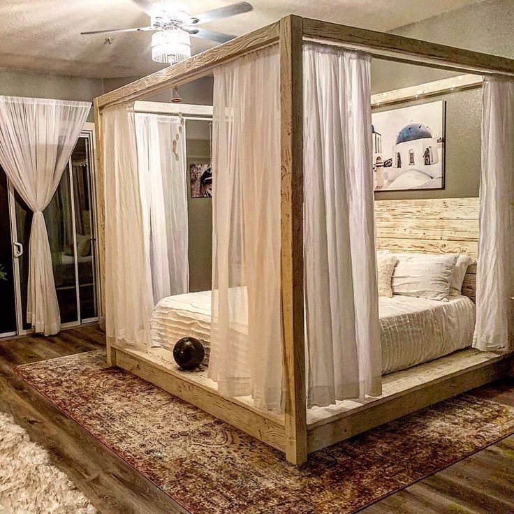 a four poster bed with white drapes and curtains on the sides, in a bedroom