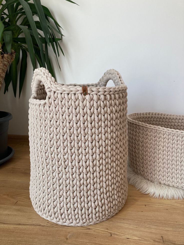 two knitted baskets sitting on top of a wooden floor next to a potted plant