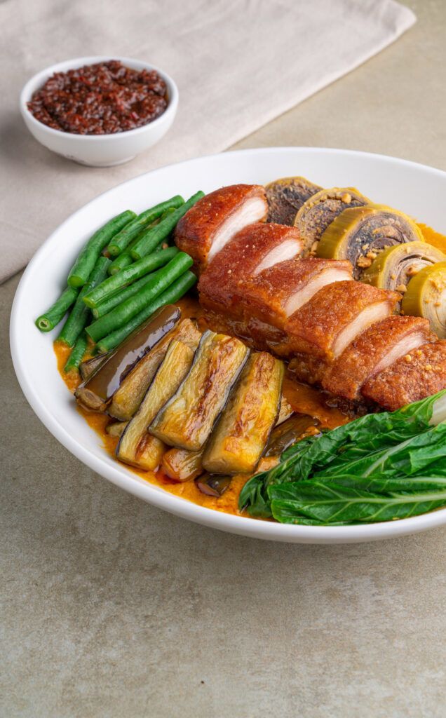 a white plate topped with meat covered in sauce and veggies next to a bowl of beans