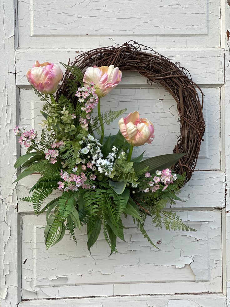 a wreath with pink flowers and greenery is hanging on a white painted wooden door