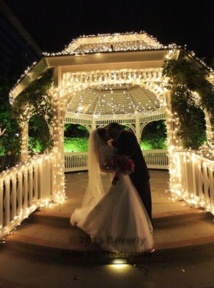 a bride and groom kissing under a gazebo covered in christmas lights